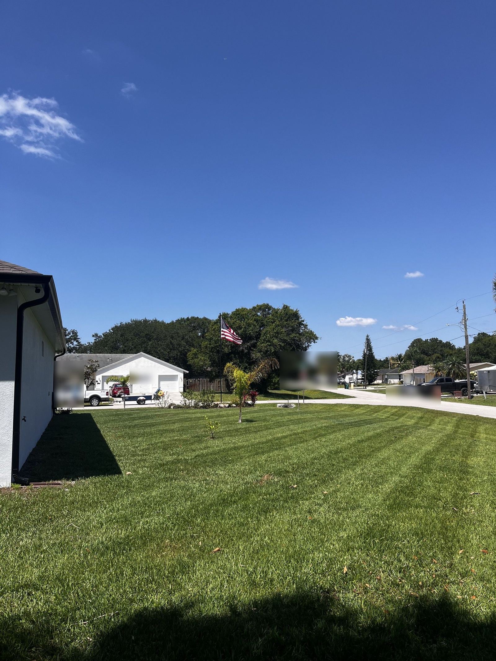 Well-maintained residential lawn with striped grass pattern, white building and American flag in background under clear blue sky.